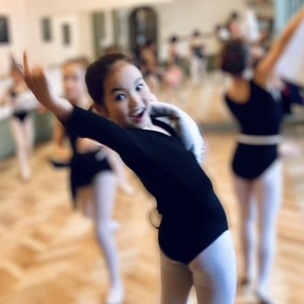 Children doing ballet in the summer at Summerschool Den Haag. One student makes a move reaching out with her hand and is smiling.