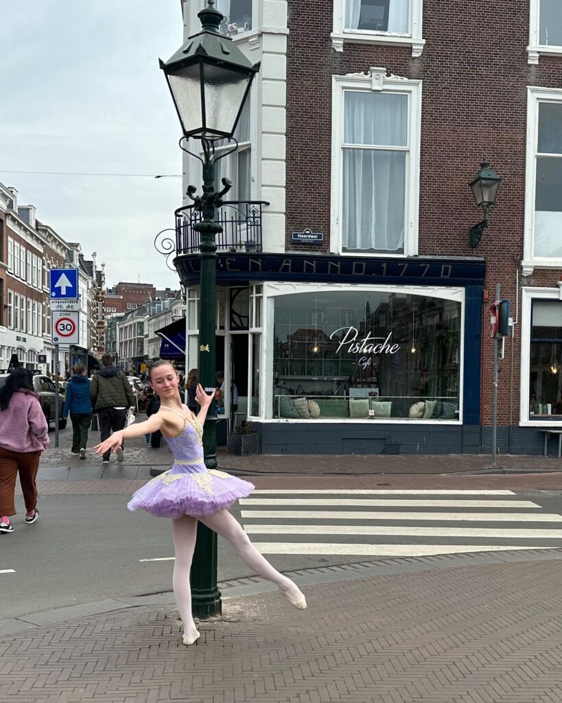 Ballet student in tutu performing a degage at a lamppost on Prinsestraat, The Hague