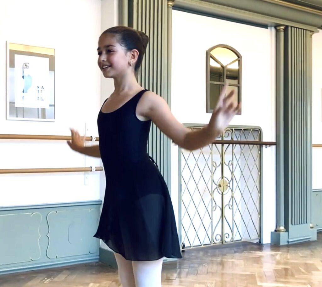 Ballet student wearing a skirt on demi-pointe reaching gracefully with arms during Youth Ballet at Summerschool Den Haag.