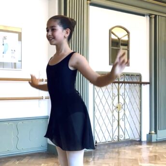 Ballet student wearing a skirt on demi-pointe reaching gracefully with arms during Youth Ballet at Summerschool Den Haag.
